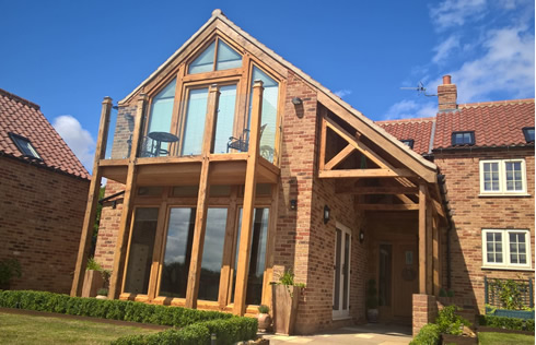 New house, Hough on the Hill. A full gable frame with Romeo and Juliet Balcony. Also side porch with Mono Trusses, all constructed from Green Oak and European Oak finished with Danish Oil.